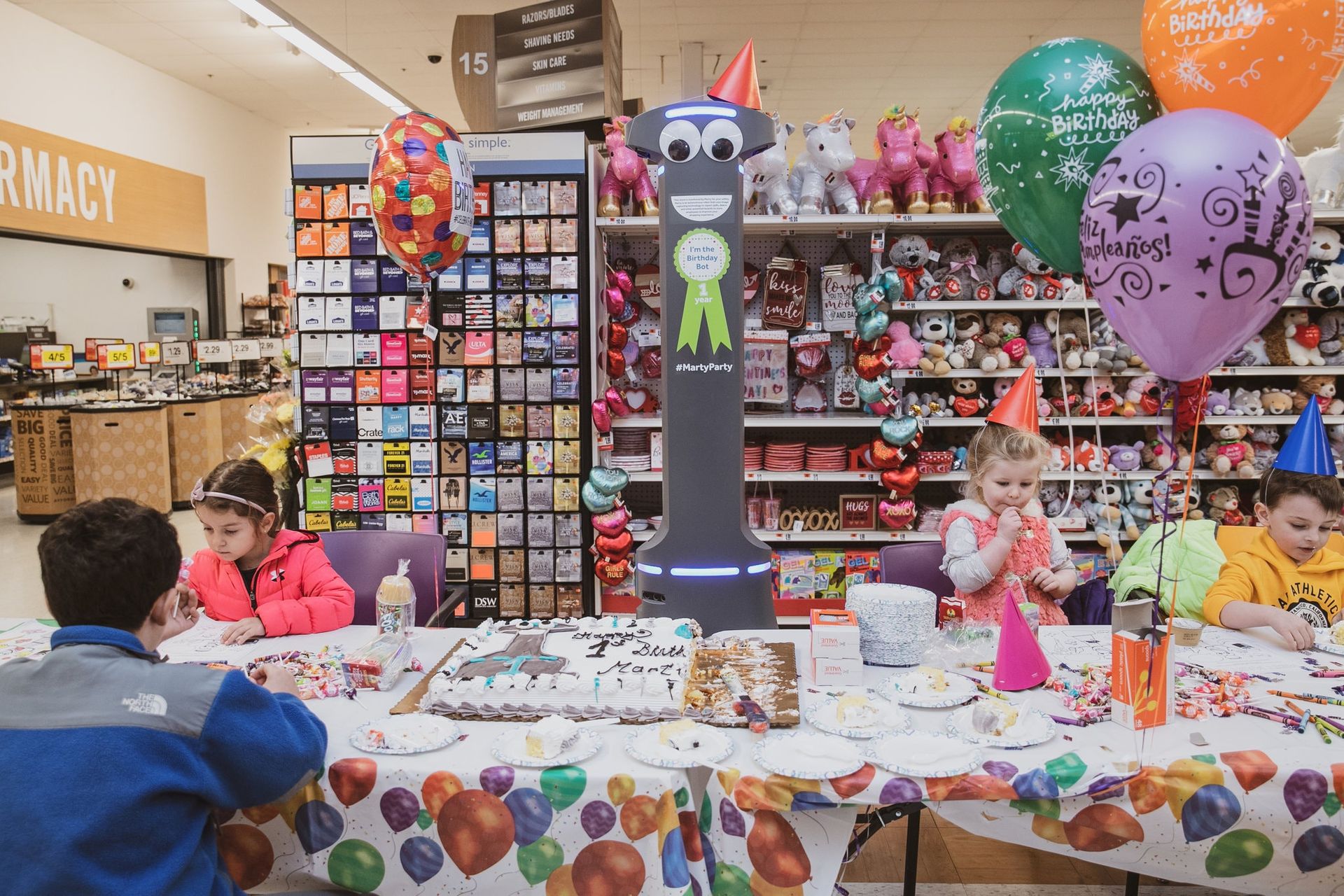 Photograph of arobot smiling over a children's party ^caption: A party to celebrate Marty, a floor cleaning robot’s, first birthday last month at the Stop & Shop in Yonkers, N.Y., via Should Robots Have a Face? - The New York Times